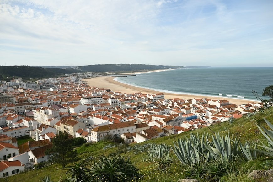 Coastal town with terracotta roofs beside a long sandy beach and ocean.