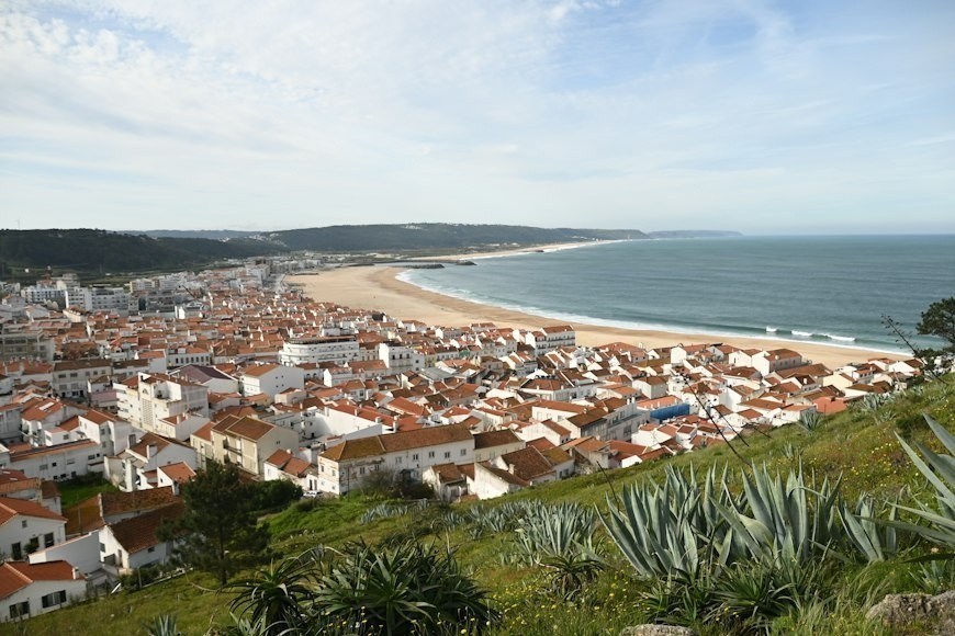 Coastal town with terracotta roofs beside a long sandy beach and ocean.