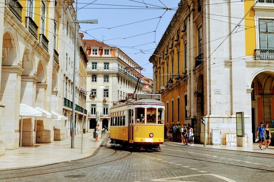 Yellow tram on a street between historic buildings in a city.