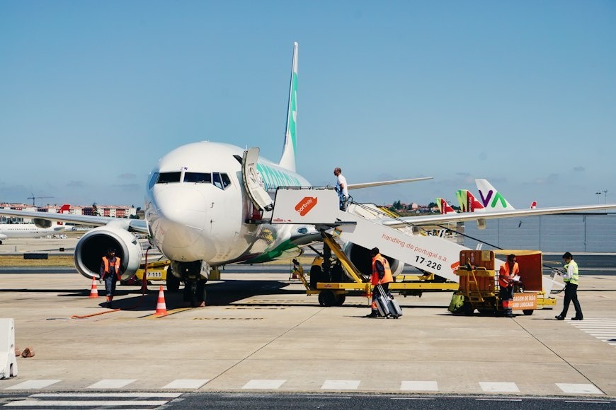 Airplane on tarmac with boarding stairs and crew unloading luggage.
